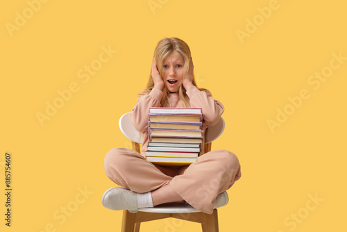 Shocked little girl with books sitting on chair against yellow background