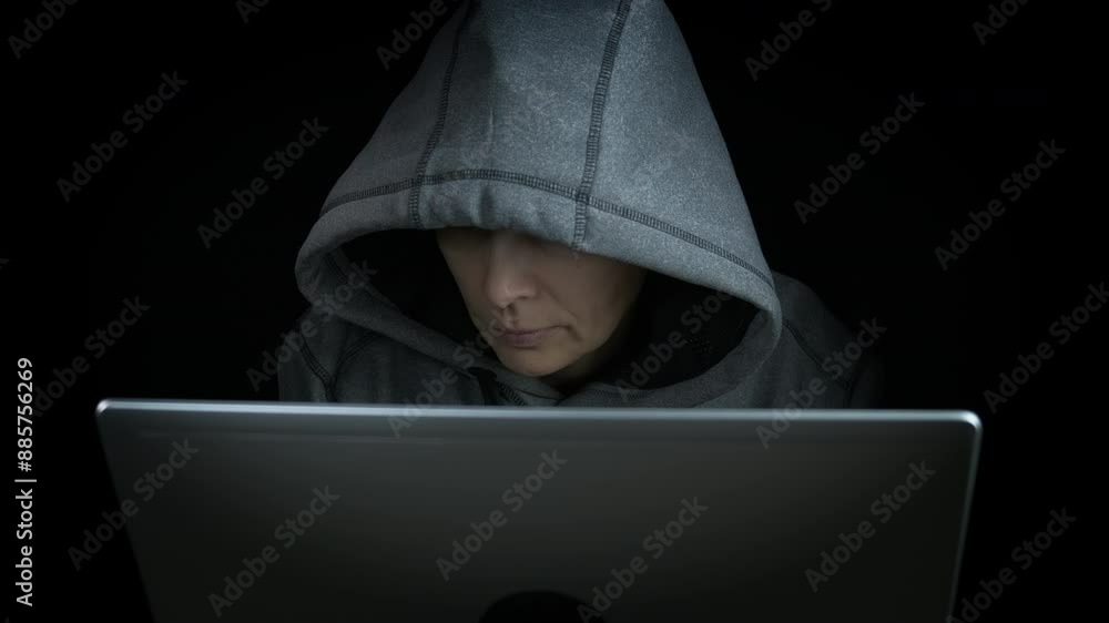 Female hacking in the internet on black background. A view of female in hoody hacking on internet by the table against black background. Female hacking in the internet on black background. A view of female in hoody hacking on internet by the table against black background.
