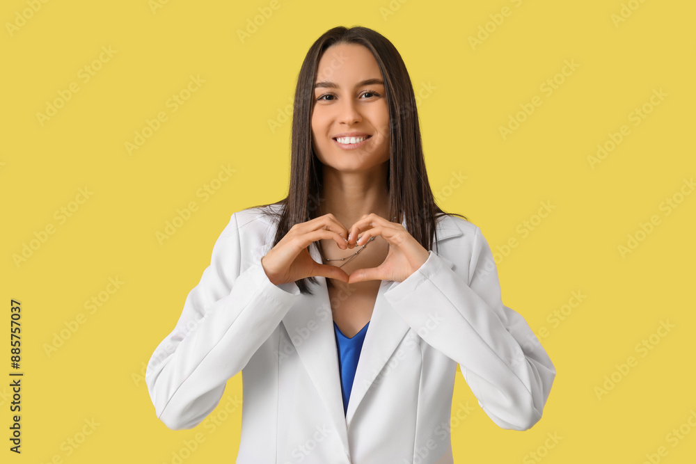 Beautiful young woman showing heart gesture on yellow background. Valentine's Day celebration Beautiful young woman showing heart gesture on yellow background. Valentine's Day celebration