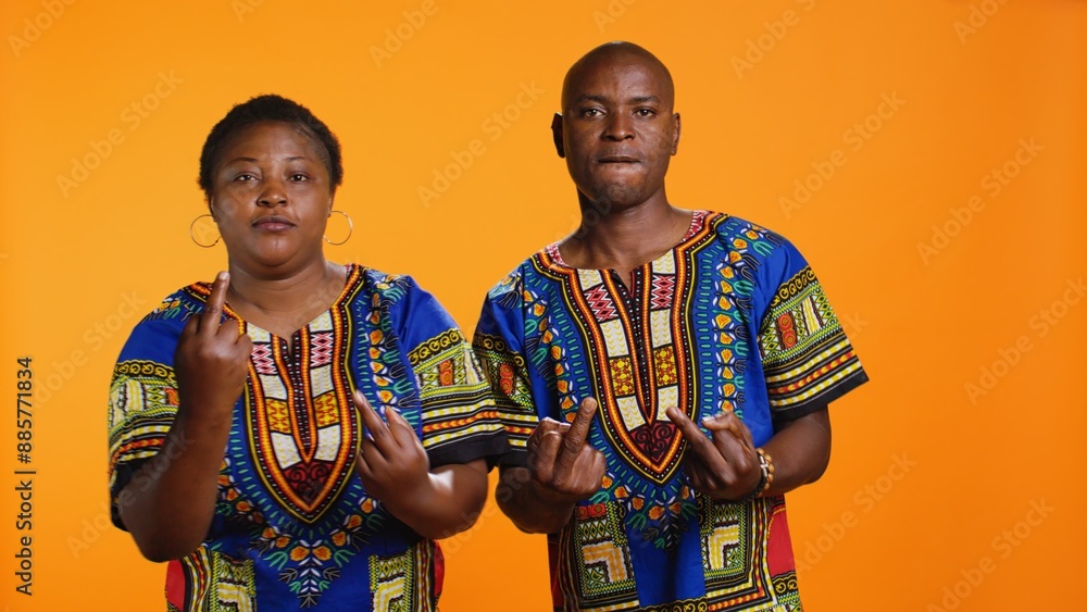 Obraz premium Provocative ethnic couple show middle finger on camera, doing offensive hooligan gesture in studio and causing fight. African american man and woman acting rude and aggressive.
