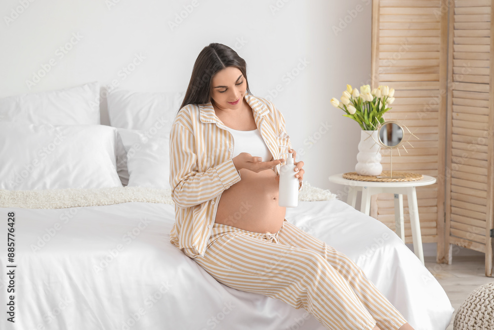Young pregnant woman with bottle of cream sitting in bedroom Young pregnant woman with bottle of cream sitting in bedroom