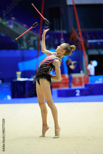 Talented young gymnast showcasing skill with clubs in graceful routine at rhythmic gymnastics event.