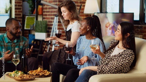 Canvas Print Portrait of smiling asian woman assisting to interesting conversation between BIPOC apartment party guests