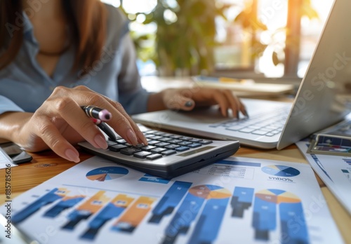 Female hands using a calculator to spatilize and tabulate financial graphs on a desk, depicting a business concept of budgeting money near a laptop computer in an office Generative AI