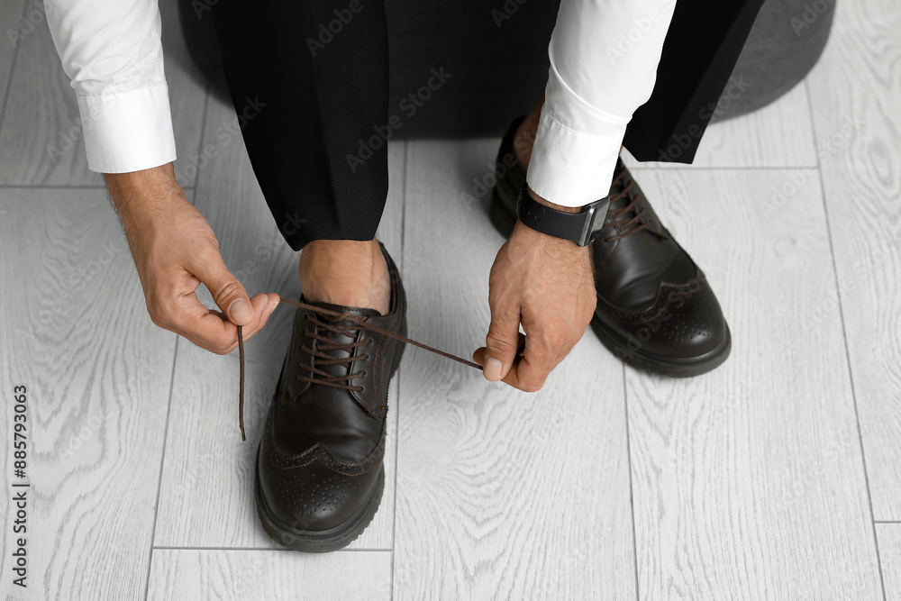 Stylish young businessman tying shoe laces at home, closeup Stylish young businessman tying shoe laces at home, closeup
