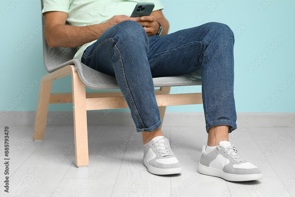 Young man in stylish sneakers sitting on chair near blue wall, closeup Young man in stylish sneakers sitting on chair near blue wall, closeup
