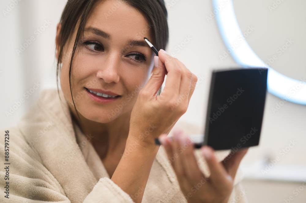 Pretty young woman looking in the mirror and making her eyebrows Pretty young woman looking in the mirror and making her eyebrows