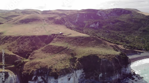 aerial panorama of beautiful nape nape beach in north canterbury, new zealand; black sand beach with turquoise water and large white cliffs, idyllic scenery with little house at the top of the cliff photo