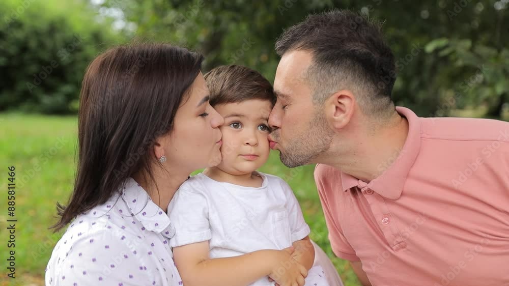 Beautiful father and mother kiss their little son, background of green trees. Happy family concept. Beautiful father and mother kiss their little son, background of green trees. Happy family concept.