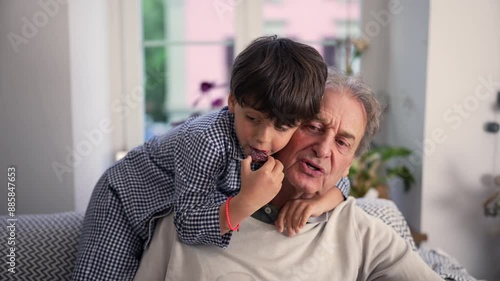 Wallpaper Mural Young boy hugging his grandfather while eating a snack, sharing a moment of affection and bonding on a sofa at home Torontodigital.ca