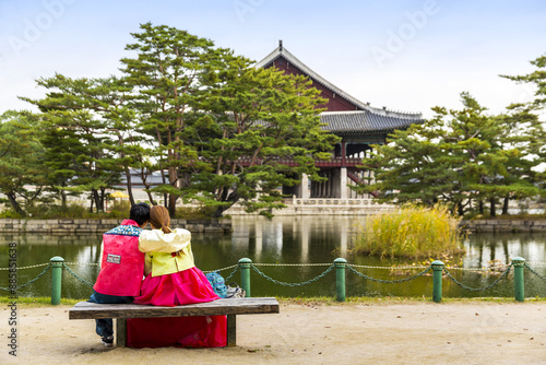 Jongno-gu, Seoul, South Korea - November 6, 2016: Back view of a couple in Korean traditional clothes sitting on bench against pond and Gyeonghoeru pavilion at Gyeongbokgung Palace
 photo