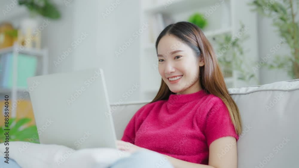Happy young Asian woman using laptop while seated on couch at home Happy young Asian woman using laptop while seated on couch at home