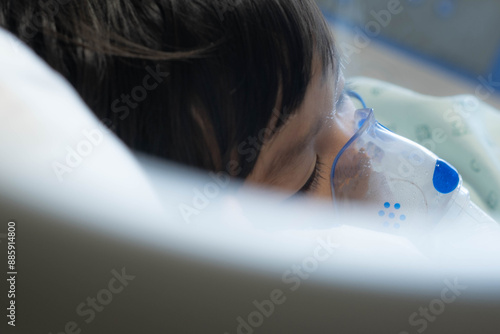 an Asian toddler boy has Cold or Flu or influenza or asthma or pneumonia disease and need nebulizations,Sick boy rest on patient bed in hospital and has inhalation therapy by the mask of inhaler.Sick 