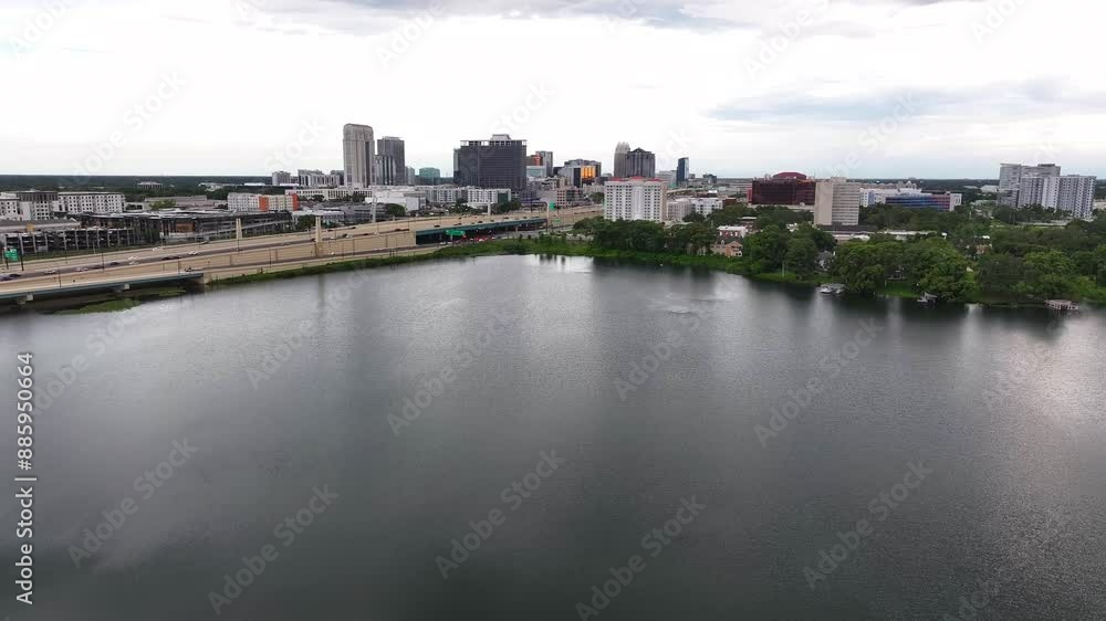 Rising drone wide shot of traffic on highway overpasses Downtown of Orlando City, USA. Tranquil lake in foreground. Cloudy day in american town, USA. Rising drone wide shot of traffic on highway overpasses Downtown of Orlando City, USA. Tranquil lake in foreground. Cloudy day in american town, USA.