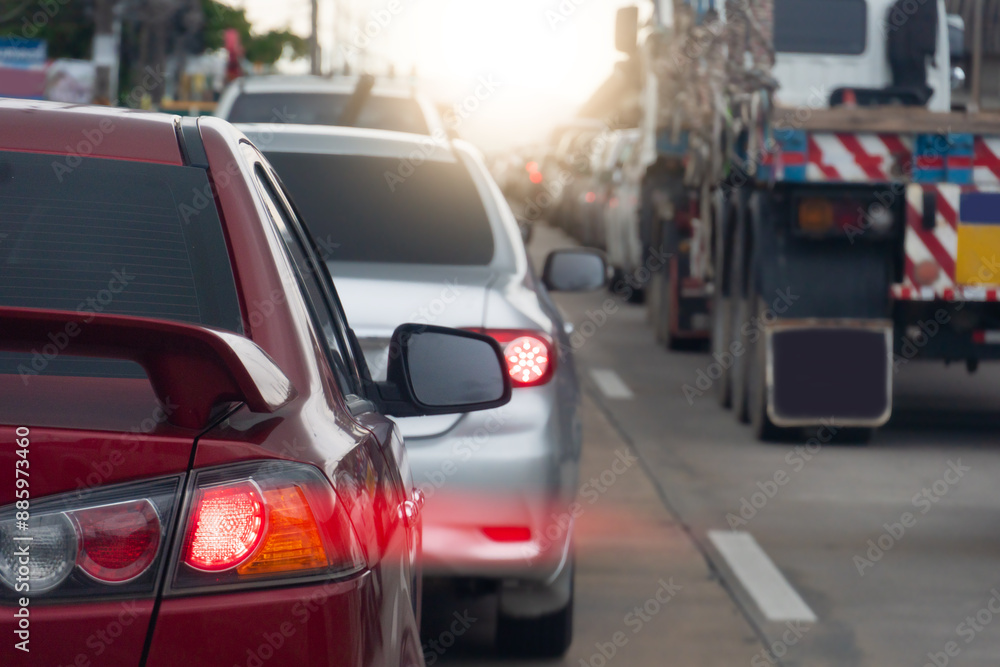 Rear side of red car on the road. Concrete road with many car during time on traffic jam. Speed light lines on the tail lights. Car parked in a long queue. Rear side of red car on the road. Concrete road with many car during time on traffic jam. Speed light lines on the tail lights. Car parked in a long queue.
