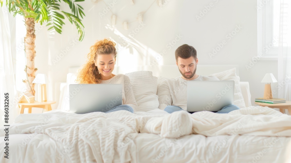Couple working on laptops while sitting on a bed in a bright, cozy room with soft morning light, blending work and relaxation. Couple working on laptops while sitting on a bed in a bright, cozy room with soft morning light, blending work and relaxation.