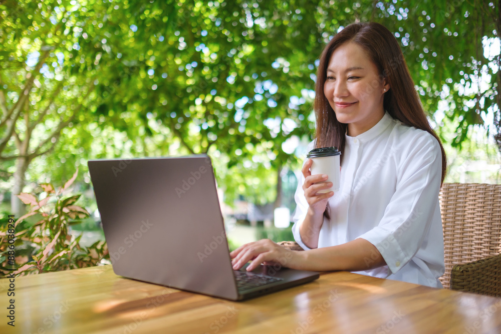 Portrait image of a woman drink coffee while working on laptop computer in the outdoors Portrait image of a woman drink coffee while working on laptop computer in the outdoors