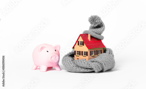 thermal insulation of buildings saves money: small model house with grey knitted scarf and cap, white background