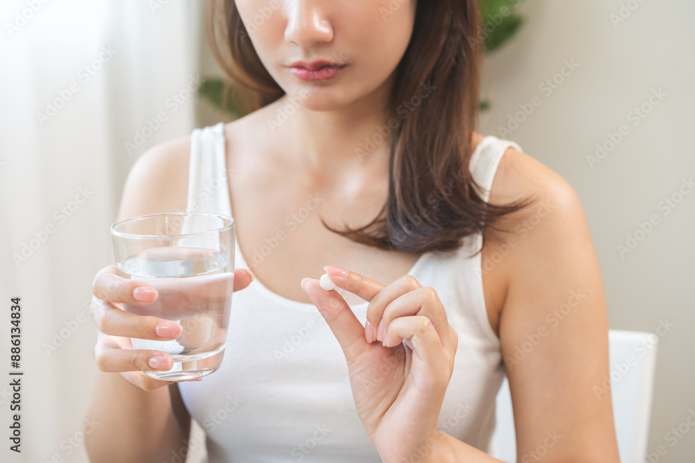 Sick asian young woman, girl holding tablet pill on hand, painkiller medicine from fever, stomach pain, headache for treatment, take drug or vitamin with glass of water at home. Health care concept. Sick asian young woman, girl holding tablet pill on hand, painkiller medicine from fever, stomach pain, headache for treatment, take drug or vitamin with glass of water at home. Health care concept.