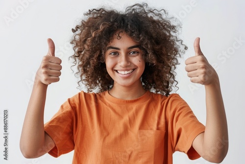 Happy Young Woman with Curly Hair Giving Thumbs Up and Smiling in Orange Shirt photo