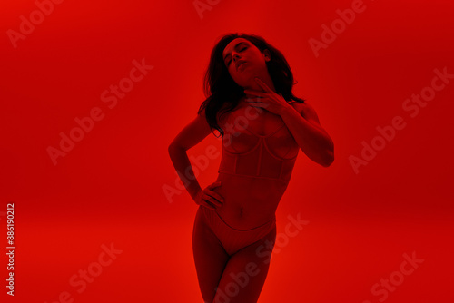Young woman confidently stands in lingerie against vibrant red backdrop. © LIGHTFIELD STUDIOS