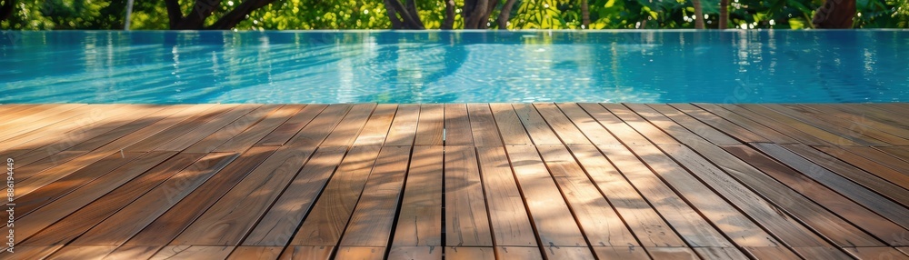 Obraz premium Serene image of a wooden deck next to a clear swimming pool with lush greenery in the background, perfect for vacation and relaxation themes.
