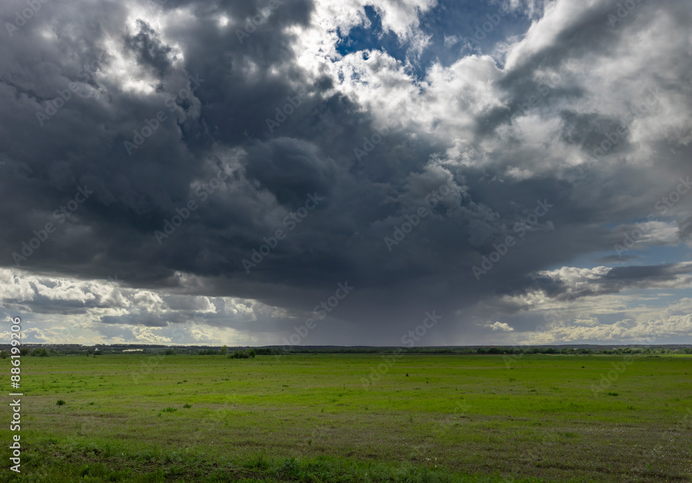 Dark, ominous storm clouds hang low over a vast green field, promising rain. Sunlight peeks through the edges of the clouds, creating a dramatic contrast against the vibrant green landscape.. Dark, ominous storm clouds hang low over a vast green field, promising rain. Sunlight peeks through the edges of the clouds, creating a dramatic contrast against the vibrant green landscape..