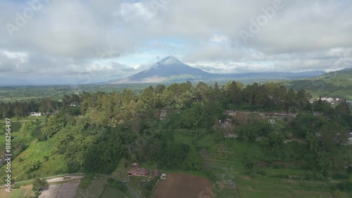 Mount Sinabung at the distance. Beautiful scenic aerial view of the green mountain side living with sun rays covered by the moving clouds. photo