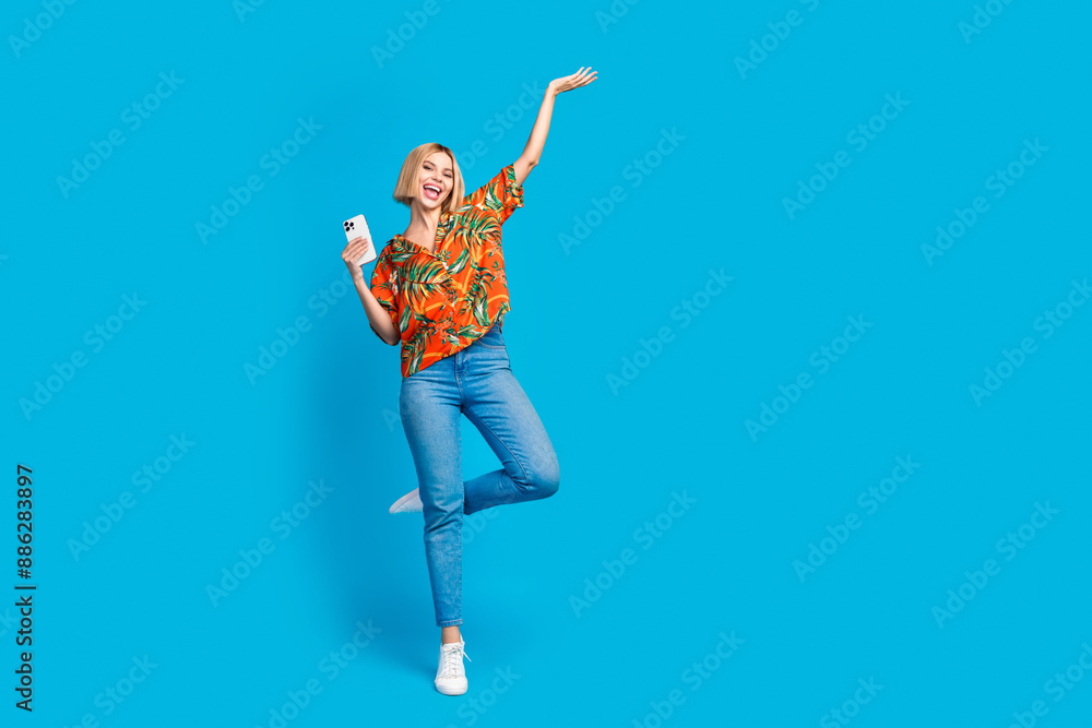 Photo of positive funky nice girl wear stylish summer print clothes hold device empty space isolated on blue color background Photo of positive funky nice girl wear stylish summer print clothes hold device empty space isolated on blue color background