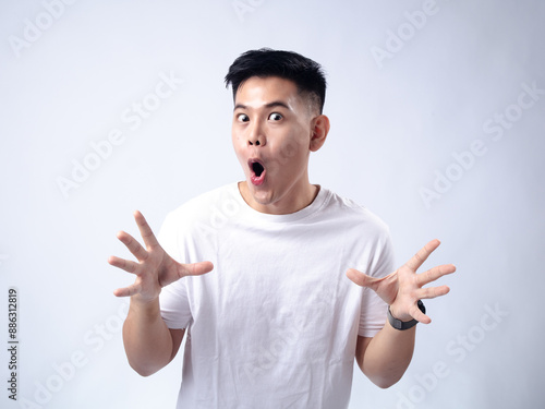 Принти на полотні A young Asian man, wearing a white shirt and black watch, has a surprised and exaggerated expression with his mouth open and hands spread wide