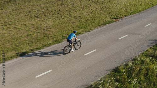 Side view of a male professional racing bike rider cycling on a paved road on a summer sunny day, aerial drone shot.