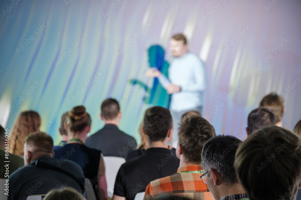 Obraz premium Group of people attending a business presentation, focusing on the speaker at the front of the room. Professional setting for corporate or educational event.