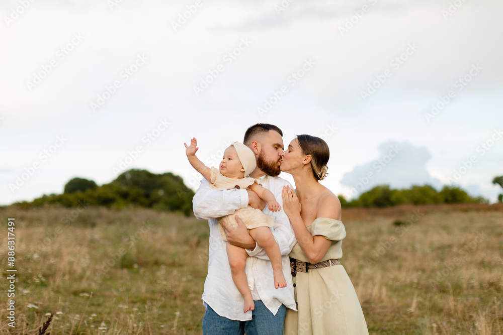 Happy family with a baby in nature. A woman in mint dress and a bearded man in white skirt are kissing and holding a baby girl in a beige dress in a field. Family, lifestyle concept. Happy family with a baby in nature. A woman in mint dress and a bearded man in white skirt are kissing and holding a baby girl in a beige dress in a field. Family, lifestyle concept.