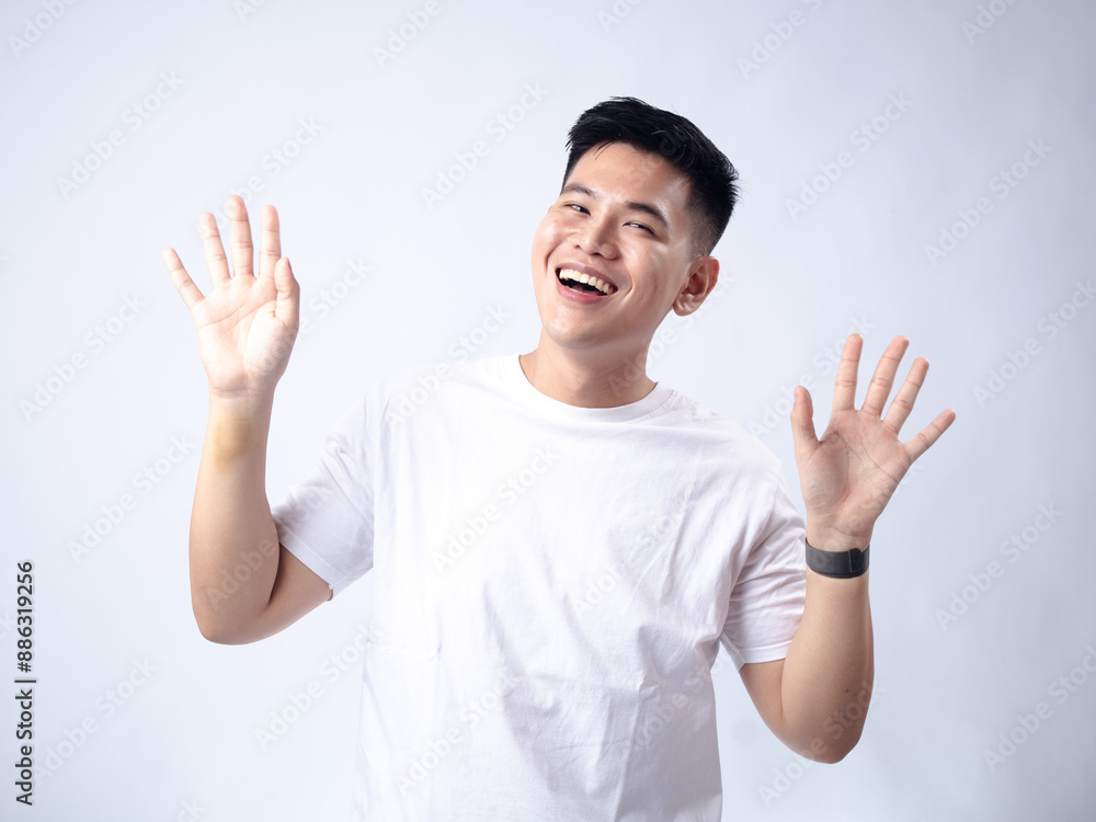 A young Asian man, wearing a white shirt and black watch, has a surprised and exaggerated expression with his mouth open and hands spread wide. The plain white background highlights A young Asian man, wearing a white shirt and black watch, has a surprised and exaggerated expression with his mouth open and hands spread wide. The plain white background highlights