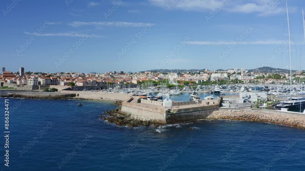 Aerial shot of the Harbor of Antibes, France in the French Riviera on a sunny summer afternoon revealing the bulwark, beach, old town, the ferris wheel and the statue Aerial shot of the Harbor of Antibes, France in the French Riviera on a sunny summer afternoon revealing the bulwark, beach, old town, the ferris wheel and the statue