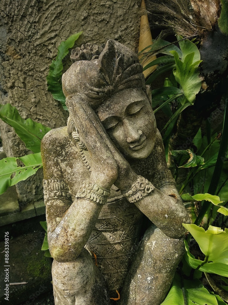 An ancient statue of a Buddhist god, in greenery, bowed its head and arms as if sleeping An ancient statue of a Buddhist god, in greenery, bowed its head and arms as if sleeping