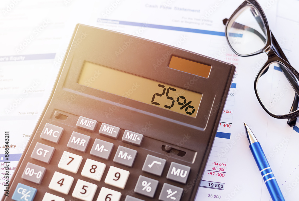 A calculator with a display showing 25% sits on a table with a financial document and glasses. A calculator with a display showing 25% sits on a table with a financial document and glasses.
