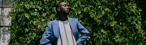 A handsome African American man with sophisticated dapper style standing in front of a vibrant green tree. photo