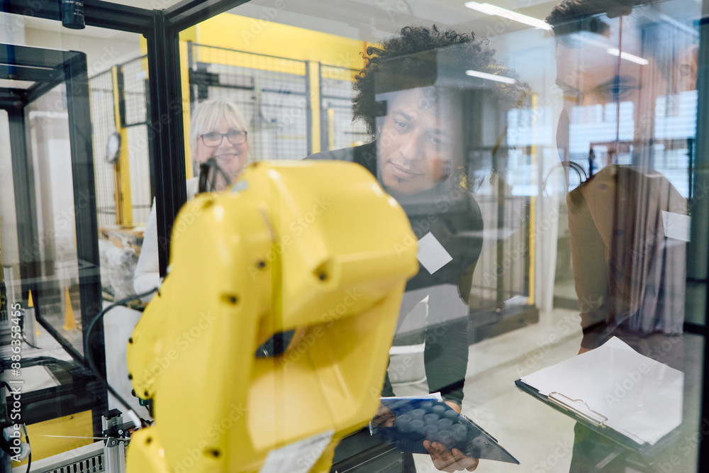 Engineers collaborating and programming robotic arm for industrial automation Engineers collaborating and programming robotic arm for industrial automation