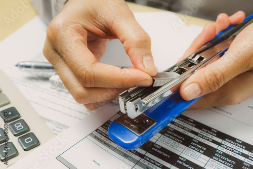 closed up woman hand refilling stapler on top of  pile of document and paper in the office table, business concept