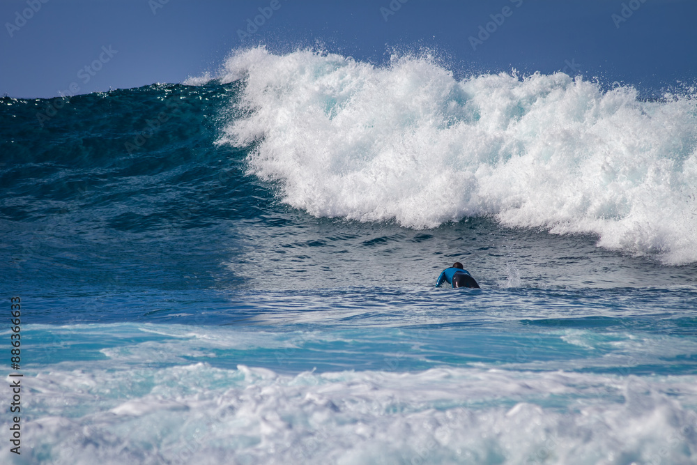 Naklejka premium Tenerife, Spain 02 11 2013: Young man surfing on a big wave with white foam. Blue sky. Surfing day. Atlantic Ocean. Tenerife, Canary Islands, Spain.