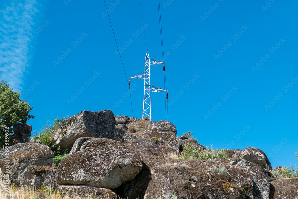 Fototapeta premium Poste elétrico de alta tensão no alto de um monte rochoso sob um céu azul