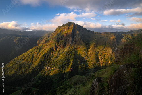 A view of a towering mountain peak surrounded by fluffy white clouds in the sky, captured in Sri Lanka.