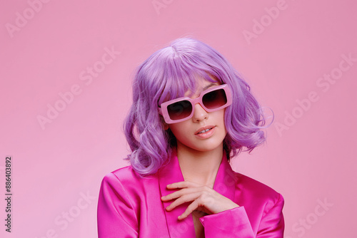 Purplehaired woman wearing sunglasses and a pink suit, posing confidently against a matching pink background © SHOTPRIME STUDIO