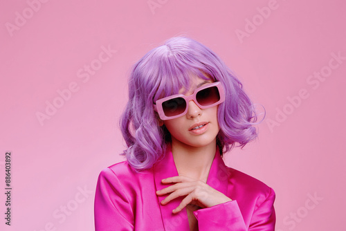 Purplehaired woman wearing sunglasses and a pink suit, posing confidently against a matching pink background photo