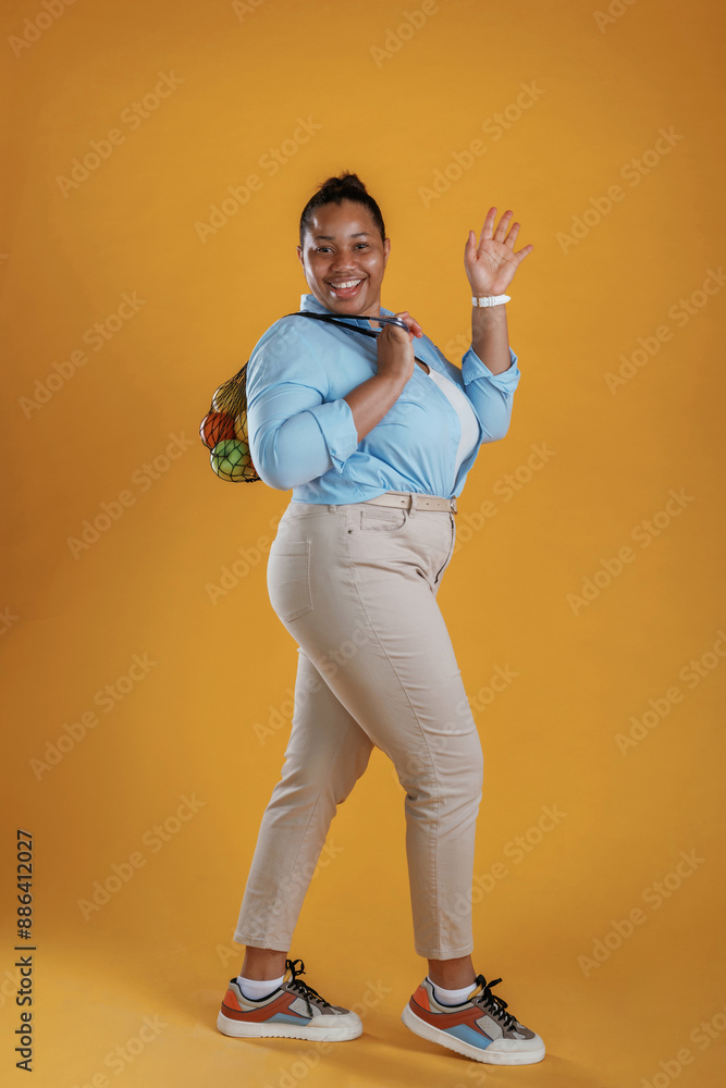 Bunch of fruits in the bag, holding. African American woman is in the studio against yellow background Bunch of fruits in the bag, holding. African American woman is in the studio against yellow background