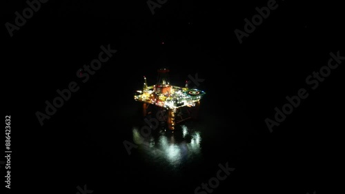 Large illuminated oil drilling rig Offshore facility for extraction of oil and gas night aerial footage downward panning far distance