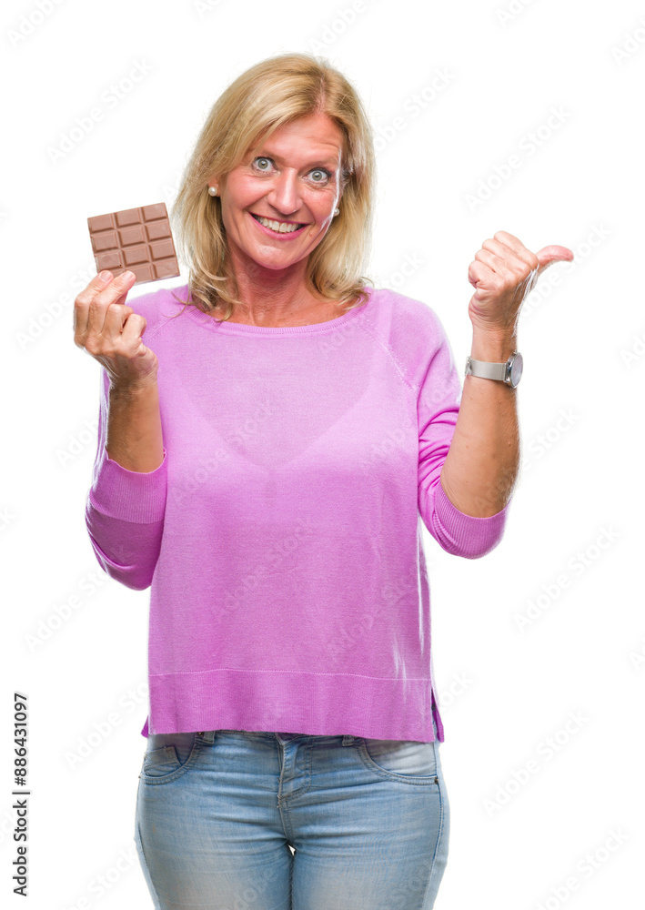Obraz premium Middle age blonde woman eating chocolate bar over isolated background pointing and showing with thumb up to the side with happy face smiling