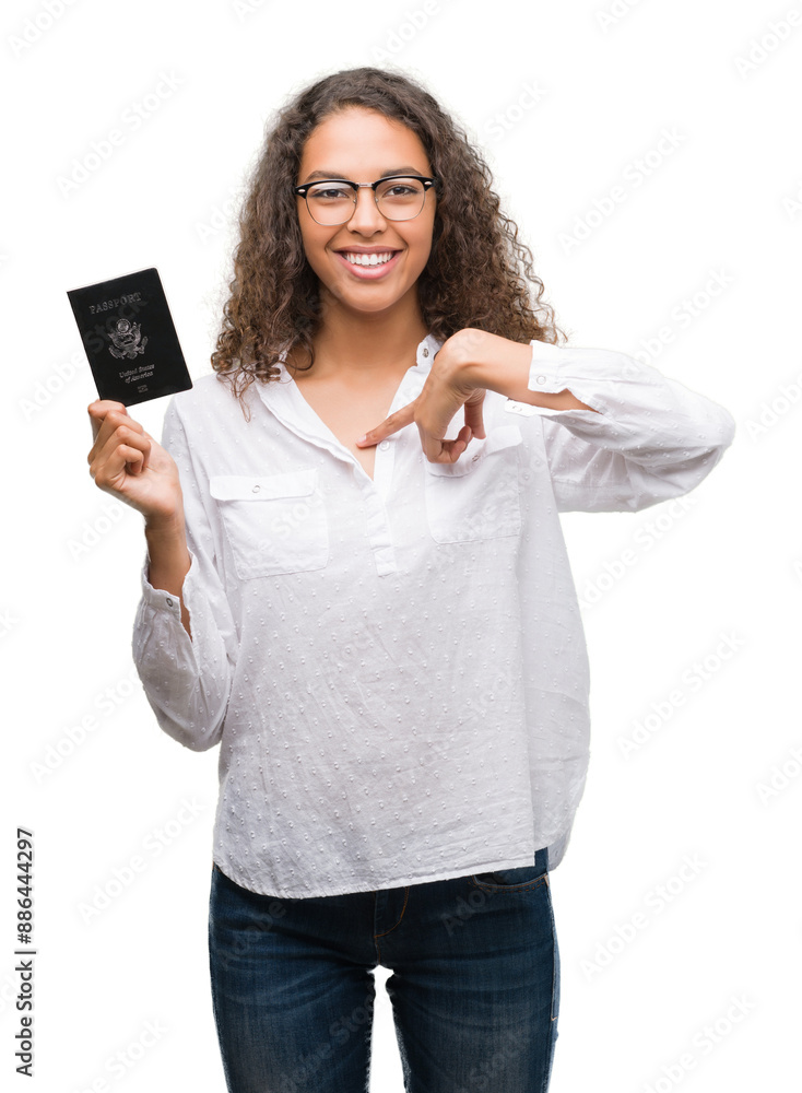Young hispanic woman holding passport of United States of America with surprise face pointing finger to himself Young hispanic woman holding passport of United States of America with surprise face pointing finger to himself
