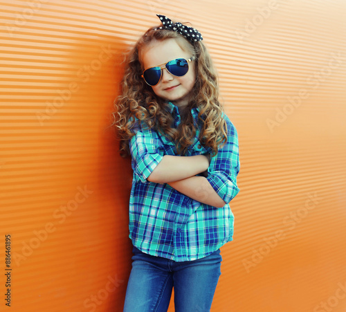 Happy kid girl with curly hair, stylish little child posing in the city on orange wall © rohappy